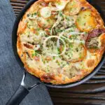 Overhead potato and onion frittata with smoked mackerel and capers in a frying pan.