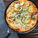 Overhead potato and onion frittata with smoked mackerel and capers in a frying pan.