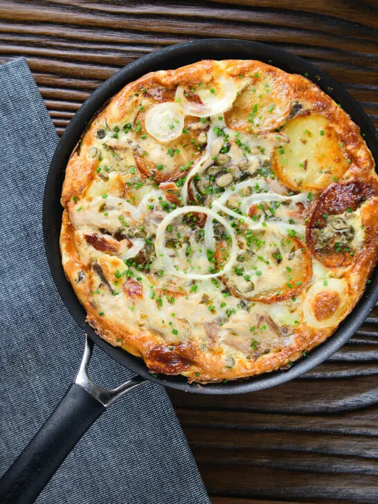 Overhead potato and onion frittata with smoked mackerel and capers in a frying pan.