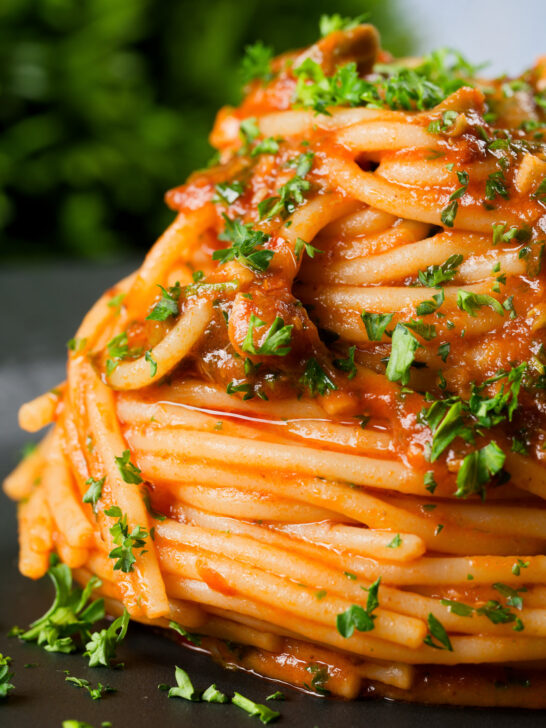 Close-up spaghetti alla puttanesca garnished with freshly chopped parsley.