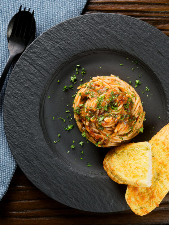 Overhead pasta puttanesca garnished with parsley served with garlic bread.