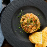 Overhead pasta puttanesca garnished with parsley served with garlic bread.