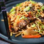 Spicy beef yakisoba noodle stir fry garnished with sesame seeds and spring onions.
