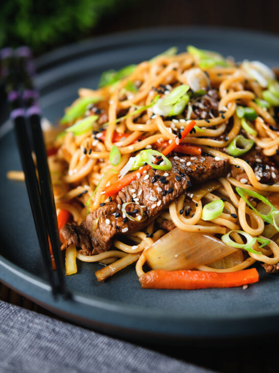 Spicy beef yakisoba noodle stir fry garnished with sesame seeds and spring onions.