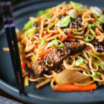 Spicy beef yakisoba noodle stir fry garnished with sesame seeds and spring onions.