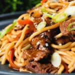 Close-up beef yakisoba noodle stir fry garnished with sesame seeds and spring onions.