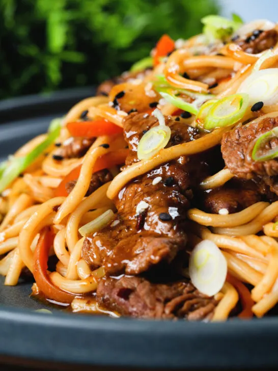 Close-up beef yakisoba noodle stir fry garnished with sesame seeds and spring onions.