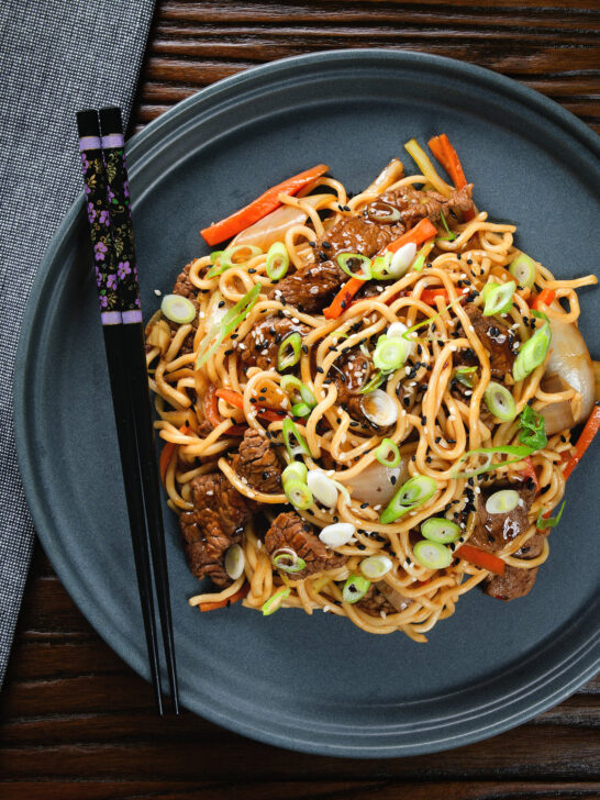 Overhead beef yakisoba noodle stir fry garnished with sesame seeds and spring onions.