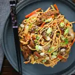 Overhead beef yakisoba noodle stir fry garnished with sesame seeds and spring onions.