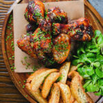 Overhead baked sticky chicken drumsticks with a cherry balsamic glaze served with wedges.