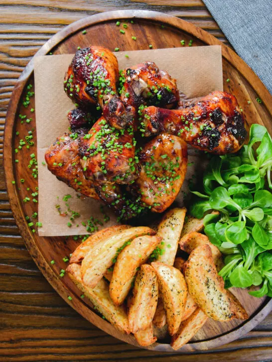 Overhead baked sticky chicken drumsticks with a cherry balsamic glaze served with wedges.