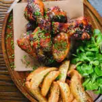 Overhead baked sticky chicken drumsticks with a cherry balsamic glaze served with wedges.