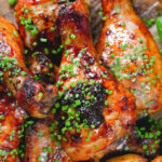 Close-up overhead baked sticky chicken drumsticks with a cherry balsamic glaze served with wedges.