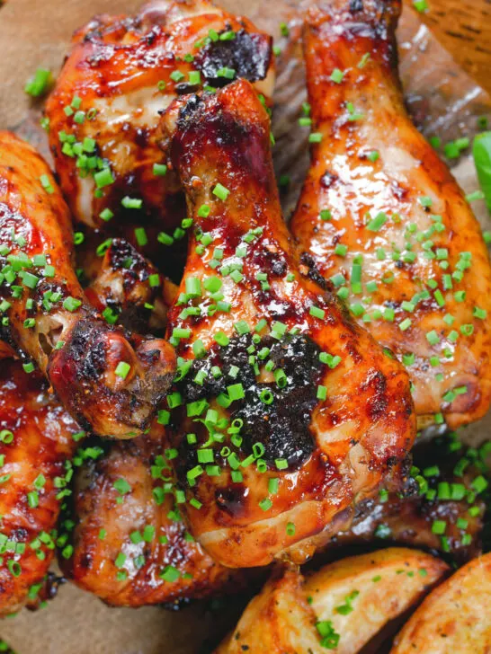 Close-up overhead baked sticky chicken drumsticks with a cherry balsamic glaze served with wedges.