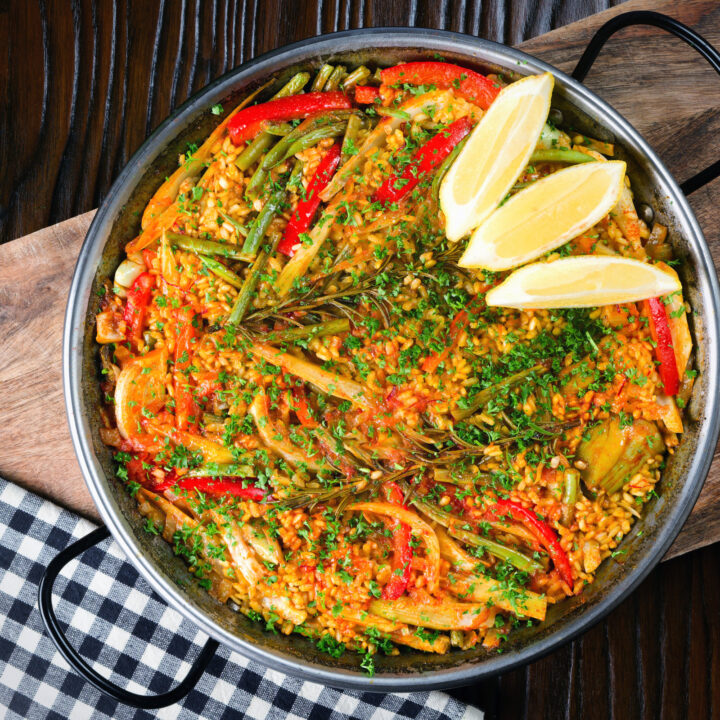 Vegetarian and vegan mixed vegetable paella served with lemon wedges.