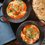 Overhead rich and creamy Indian butter chicken curry or murgh makhani served with naan bread.
