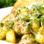 Close-up garlic chicken and basil pesto gnocchi served with cheesy garlic bread.