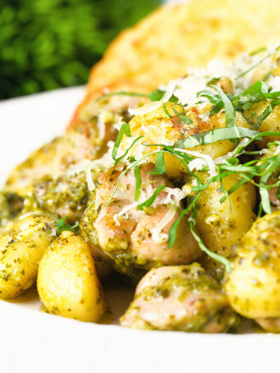 Close-up garlic chicken and basil pesto gnocchi served with cheesy garlic bread.