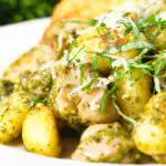 Close-up garlic chicken and basil pesto gnocchi served with cheesy garlic bread.