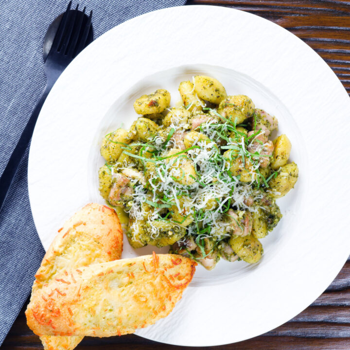 Chicken pesto gnocchi garnished with parmesan and basil served with cheesy garlic bread.