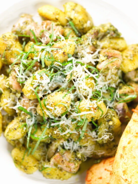 Overhead close-up garlic chicken and basil pesto gnocchi served with cheesy garlic bread.