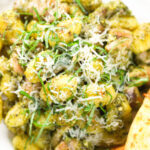 Overhead close-up garlic chicken and basil pesto gnocchi served with cheesy garlic bread.