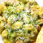 Overhead close-up garlic chicken and basil pesto gnocchi served with cheesy garlic bread.