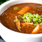 Close-up vegetarian Chinese hot and sour soup garnished with spring onions.