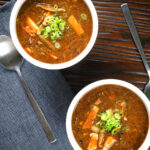 Overhead vegetarian Chinese hot and sour soup garnished with spring onions.