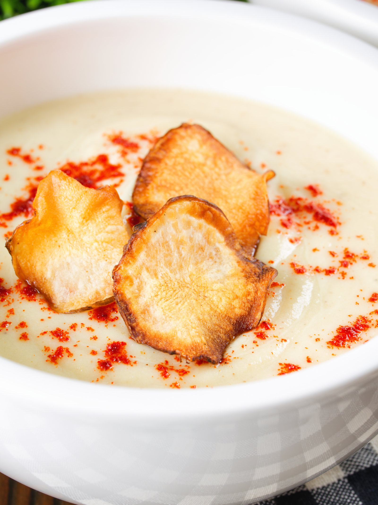 Close up Creamy Jerusalem artichoke soup garnished with paprika and fried sunchoke crisps.