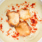 Overhead close-up creamy Jerusalem artichoke soup garnished with paprika and fried sunchoke crisps.