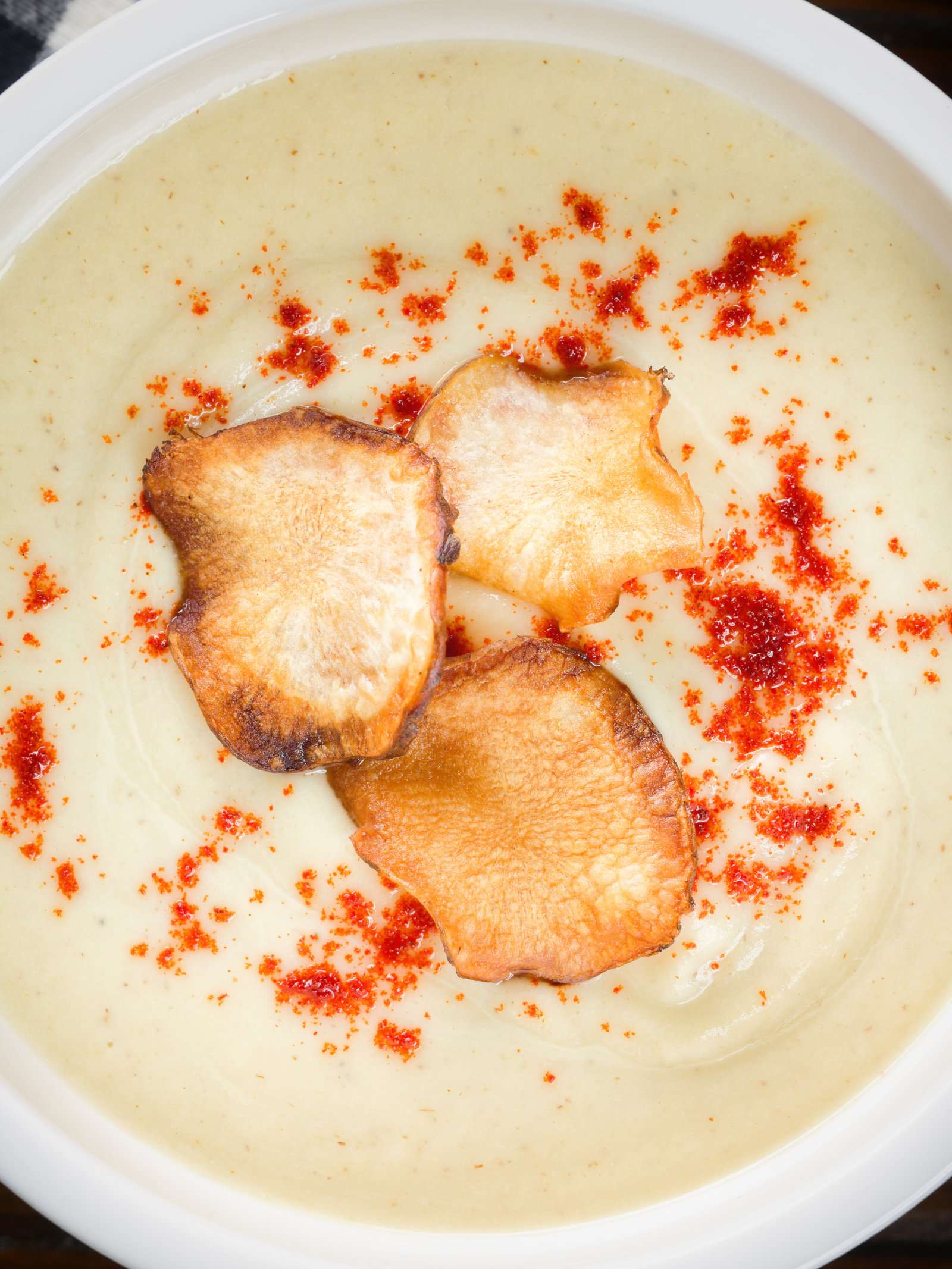 Overhead close-up creamy Jerusalem artichoke soup garnished with paprika and fried sunchoke crisps.