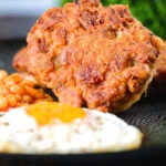 Close-up crispy canned corned beef fritters with fried egg and beans.