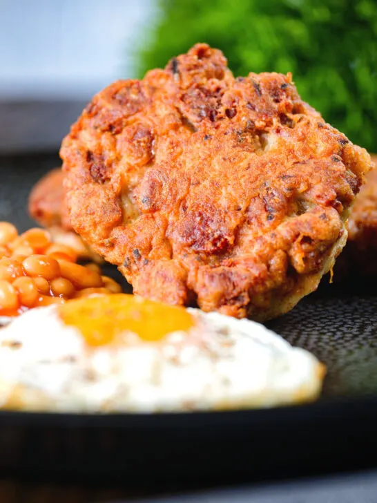 Close-up crispy canned corned beef fritters with fried egg and beans.