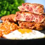 Crispy corned beef fritters cut open to show texture served with fried egg and beans.