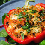 Close-up baked stuffed peppers with halloumi cheese, brown rice, harissa pasta and raisins.