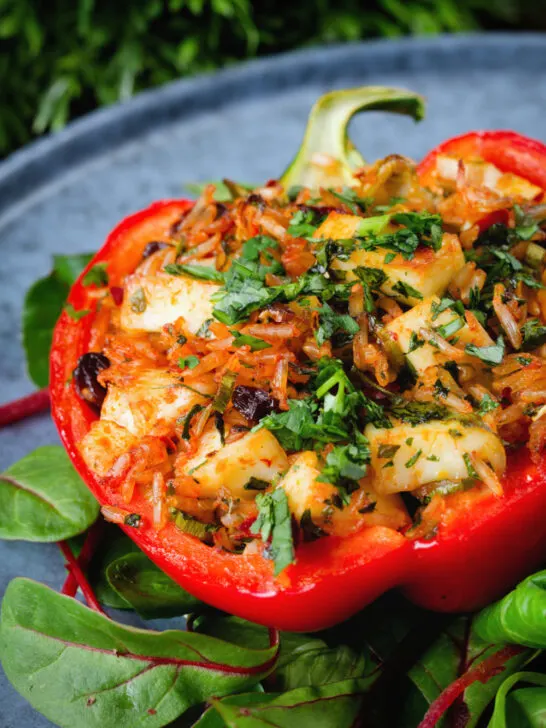 Close-up baked stuffed peppers with halloumi cheese, brown rice, harissa pasta and raisins.