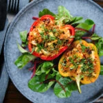 Overhead baked stuffed peppers with halloumi cheese, brown rice, harissa pasta and raisins.