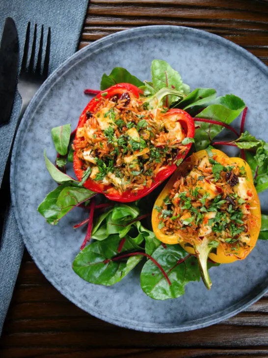 Overhead baked stuffed peppers with halloumi cheese, brown rice, harissa pasta and raisins.