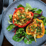 Overhead baked stuffed peppers with halloumi cheese, brown rice, harissa pasta and raisins.