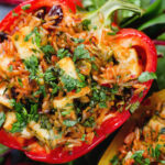 Overhead close-up baked stuffed peppers with halloumi cheese, brown rice, harissa pasta and raisins.