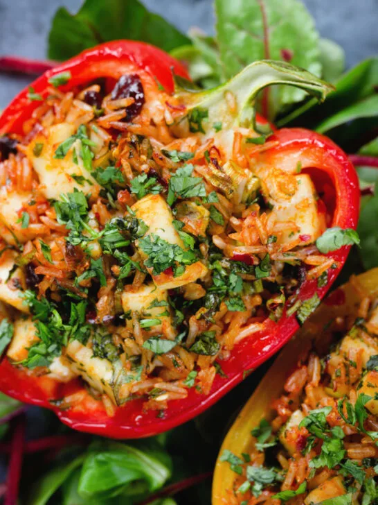 Overhead close-up baked stuffed peppers with halloumi cheese, brown rice, harissa pasta and raisins.