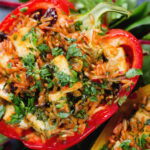 Overhead close-up baked stuffed peppers with halloumi cheese, brown rice, harissa pasta and raisins.