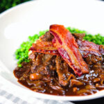 Braised liver and onions, in a rich onion gravy served with crispy bacon and peas.