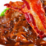 Close-up braised liver and onions, in a rich onion gravy served with crispy bacon.