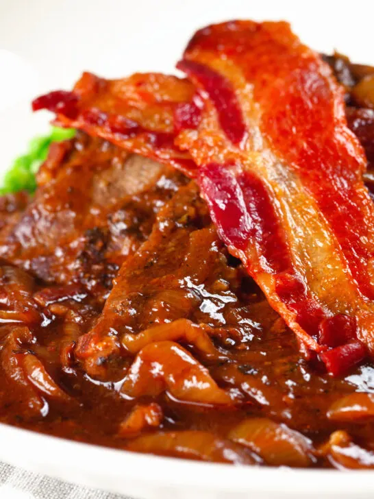 Close-up braised liver and onions, in a rich onion gravy served with crispy bacon.