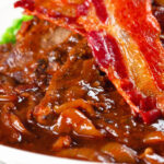 Close-up braised liver and onions, in a rich onion gravy served with crispy bacon.