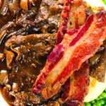 Overhead close-up liver and onions, in onion gravy served with crispy bacon, mash and peas.