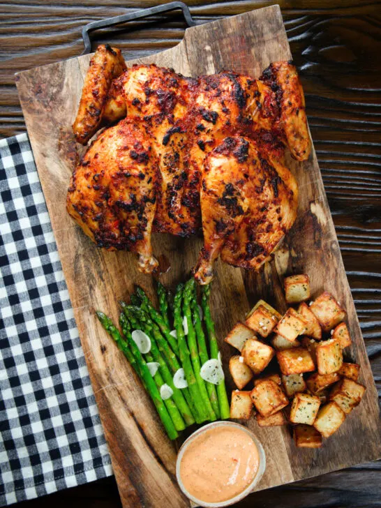 Overhead whole baked peri peri spatchcock chicken served with Parmentier potatoes and garlic asparagus.