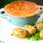 Pork and apple pie with a puff pastry lid served with buttered new potatoes and peas.